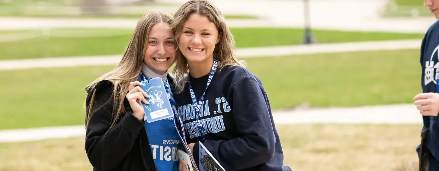 Two students posing together holding a name badge outside